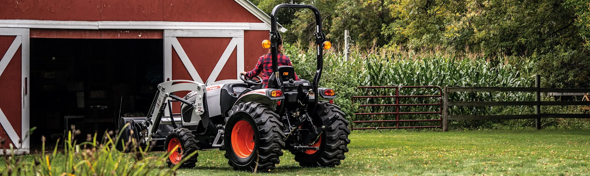 Bobcat compact tractor with a front-end loader working beside a barn