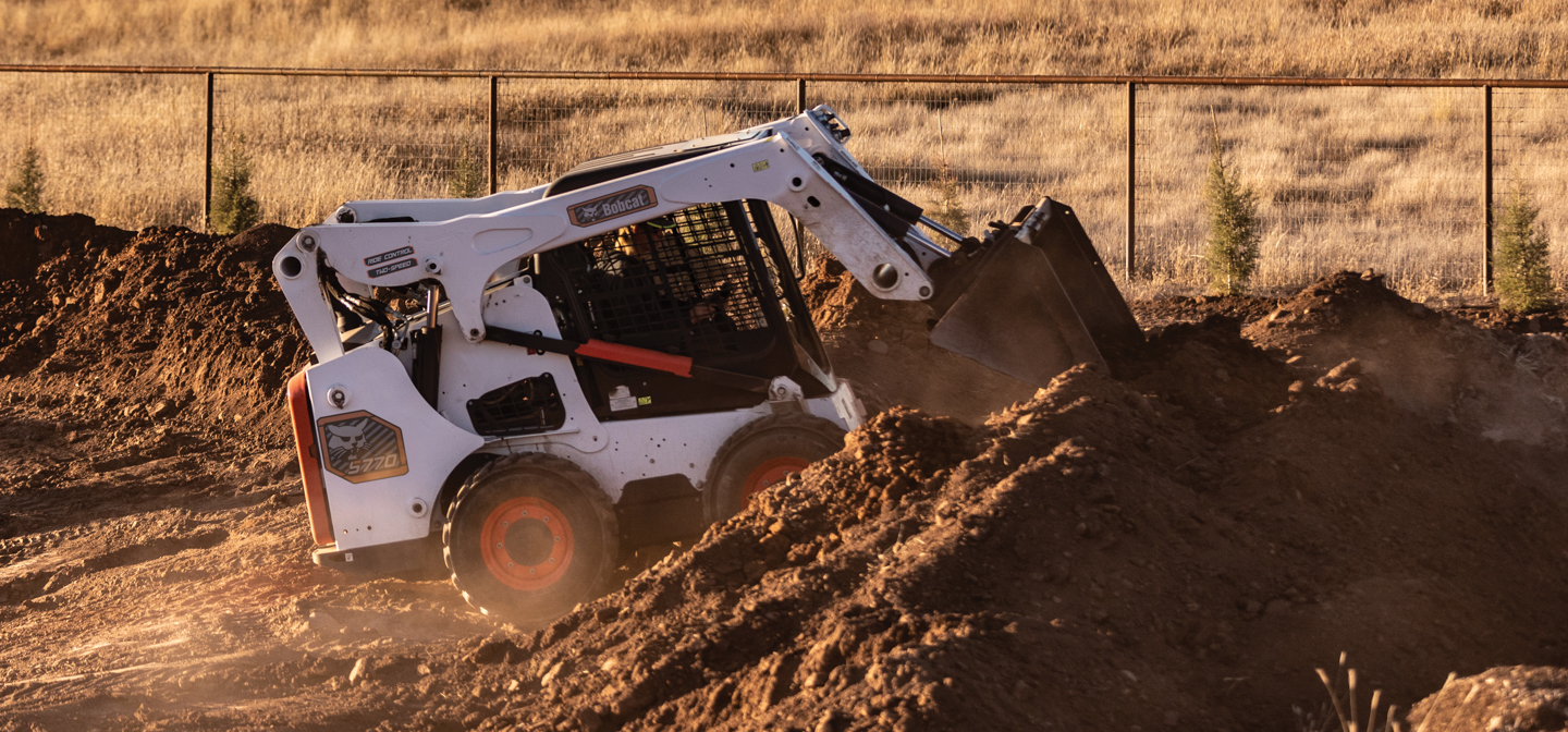 Bobcat S770 skid-steer loader digging into a dirt pile